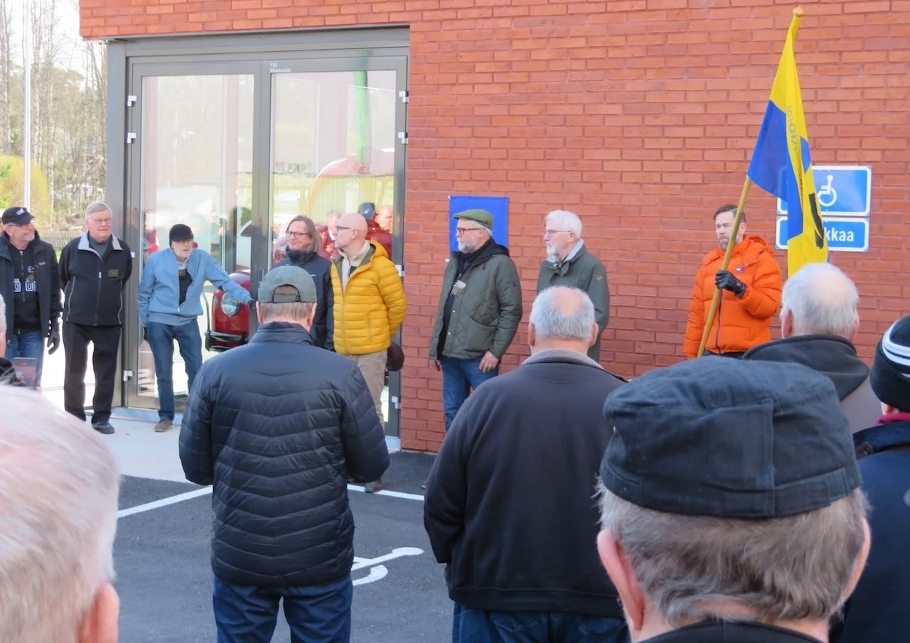 Näkymiä liiton perustamislaatan paljastustilaisuudesta Noormarkun palolaitoksen edustalla. Sininen neliö seinässä on vielä peitossa oleva laatta. Neljä Markkua laatan edessä ovat Markku-liiton perustajajäseniä. Vasemmalta Pohjanmäki, Salminen, Sandell ja Haapio. Liiton lippua pitää hallituksen jäsen Kataja.